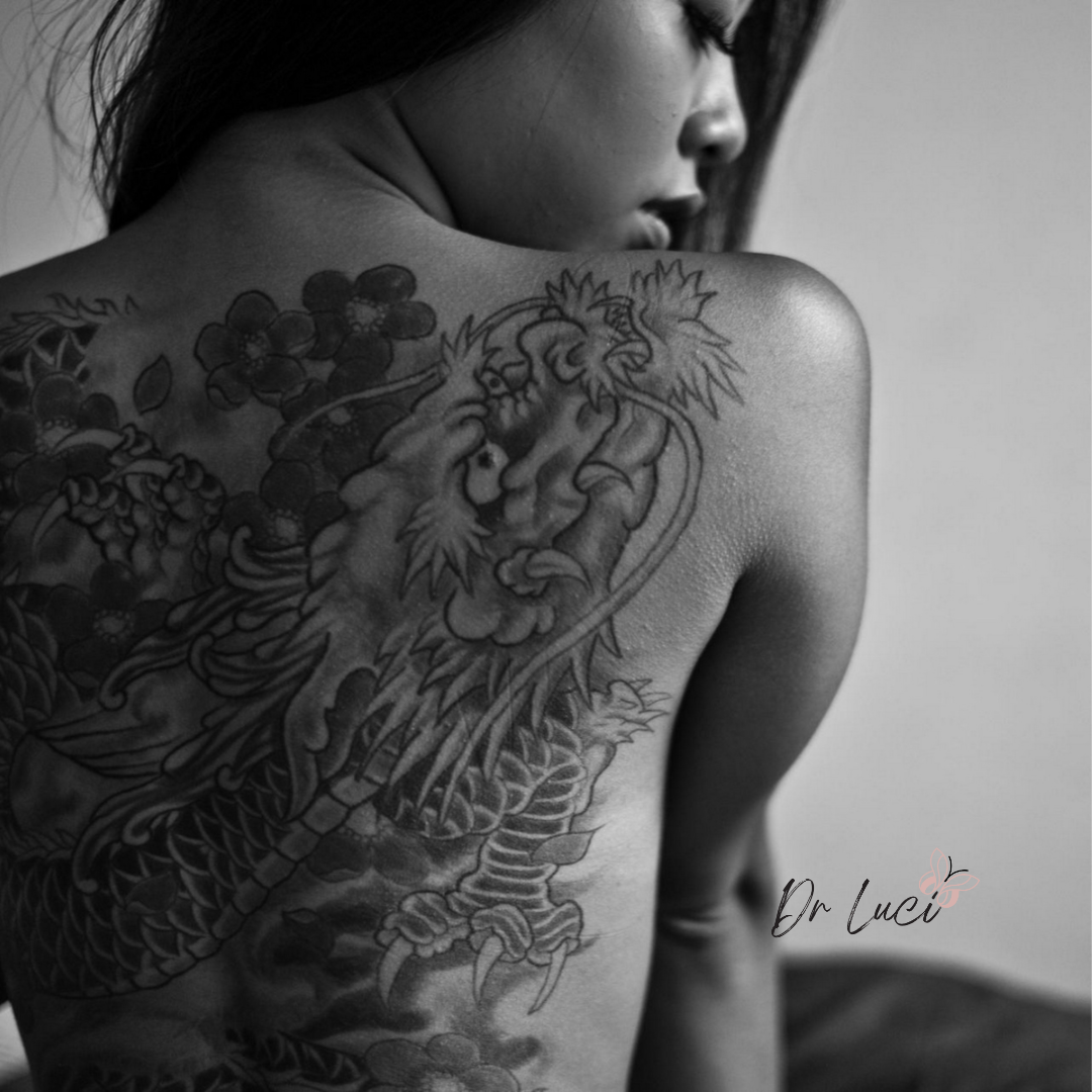 Monochrome picture of woman with whole back tattoo and dr luci clinic logo in corner